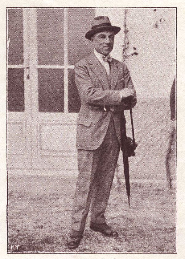 Old black-and-white photo of Federico Tesio standing outside a building in a suit, bow tie and hat, hands resting on a furled umbrella